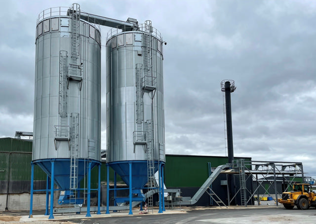 A silo with a trucklader outside of a industrial building 